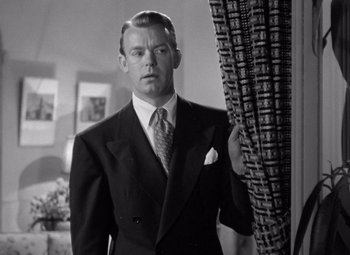 Movie still from “The Leopard Man” (1943), directed by Jacques Tourneur – A man in a suit and tie standing next to a curtain; Close Up shot, Low angle