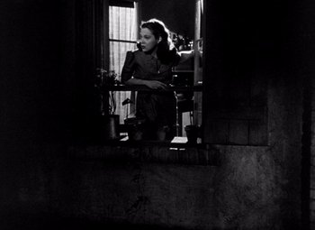 Movie still from “The Leopard Man” (1943), directed by Jacques Tourneur – A black and white photo of a woman looking out a window; Medium shot, Low angle