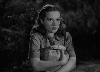 Movie still from “The Leopard Man” (1943), directed by Jacques Tourneur – A young woman holding a paper bag while standing in a forest; Close Up shot, Low angle
