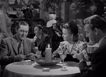 Movie still from “The Leopard Man” (1943), directed by Jacques Tourneur – A black and white photo of people sitting at a table; Medium shot, High angle