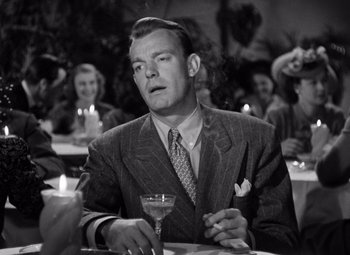 Movie still from “The Leopard Man” (1943), directed by Jacques Tourneur – A man sitting at a table with a glass in his hand; Close Up shot, Low angle