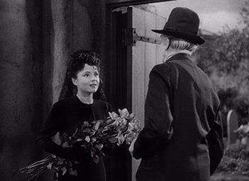 Movie still from “The Leopard Man” (1943), directed by Jacques Tourneur – An old photo of a woman holding a bunch of flowers; Medium shot, Over the shoulder angle