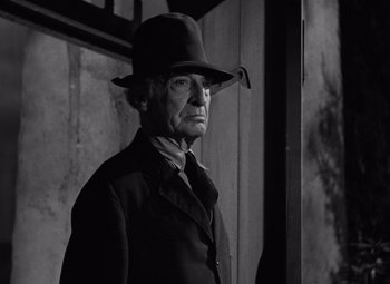Movie still from “The Leopard Man” (1943), directed by Jacques Tourneur – An old man wearing a hat standing in front of a wall; Close Up shot, Low angle