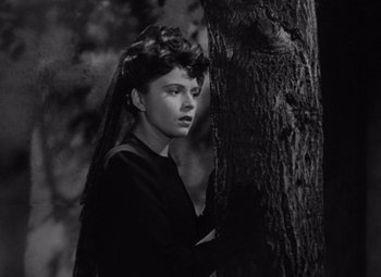 Movie still from “The Leopard Man” (1943), directed by Jacques Tourneur – A woman standing next to a tree in a forest; Close Up shot, High angle