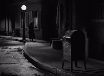 Movie still from “The Leopard Man” (1943), directed by Jacques Tourneur – A person walking down a street at night with a mailbox; Wide shot, High angle