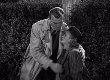 Movie still from “The Leopard Man” (1943), directed by Jacques Tourneur – An older man and a younger woman embracing each other in front of bushes; Medium shot, High angle