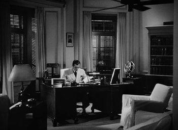 Movie still from “The Letter” (1940), directed by William Wyler – A man sitting at a desk in front of a computer; Wide shot, High angle