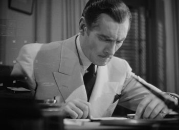 Movie still from “The Letter” (1940), directed by William Wyler – A black and white photo of a man writing on a piece of paper; Medium shot, High angle