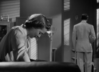 Movie still from “The Letter” (1940), directed by William Wyler – A woman sitting on a couch next to a man in a suit; Medium shot, Low angle