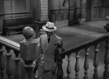 Movie still from “The Letter” (1940), directed by William Wyler – A black and white photo of a man in a suit and a hat; Wide shot, High angle