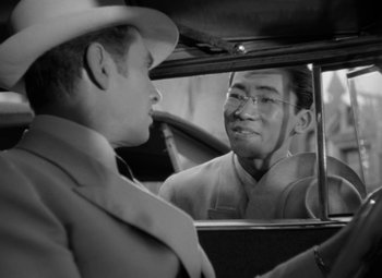 Movie still from “The Letter” (1940), directed by William Wyler – A man in a suit and hat looking at a man in a hat in a car mirror; Close Up shot, Over the shoulder angle