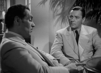 Movie still from “The Letter” (1940), directed by William Wyler – Two men in suits are talking to each other in a room; Medium shot, Over the shoulder angle