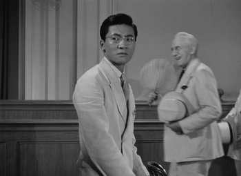 Movie still from “The Letter” (1940), directed by William Wyler – A man standing in front of another man holding an umbrella; Medium shot, Over the shoulder angle