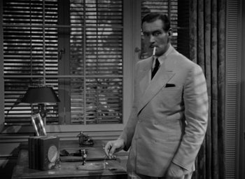 Movie still from “The Letter” (1940), directed by William Wyler – A black and white photo of a man smoking a cigarette; Medium shot, High angle