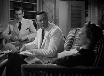 Movie still from “The Letter” (1940), directed by William Wyler – A man and a woman sitting next to each other in front of another man in a suit; Medium shot, Over the shoulder angle