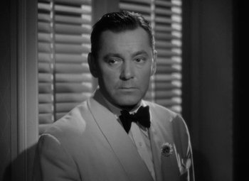 Movie still from “The Letter” (1940), directed by William Wyler – A man wearing a suit and bow tie in front of a window; Close Up shot, Low angle