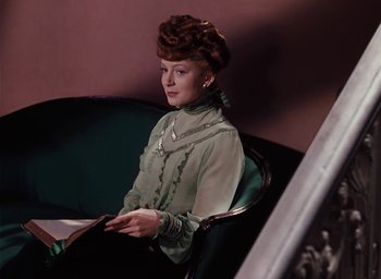 Movie still from “The Life and Death of Colonel Blimp” (1943), directed by Emeric Pressburger – A woman sitting on top of a green couch holding an open book; Medium shot, Low angle