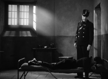 Movie still from “The Life of Emile Zola” (1937), directed by William Dieterle – A black and white photo of a man chained to a bed; Wide shot, High angle
