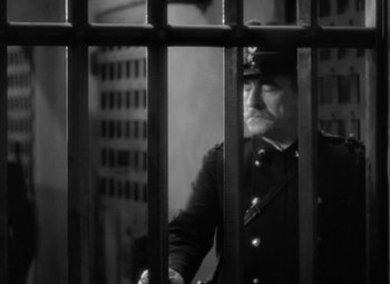 Movie still from “The Life of Emile Zola” (1937), directed by William Dieterle – A black and white photo of a man in uniform behind a fence; Medium shot, Low angle