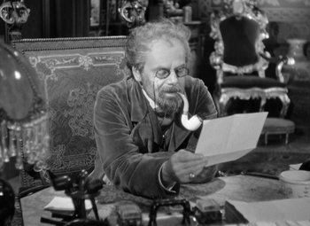Movie still from “The Life of Emile Zola” (1937), directed by William Dieterle – An older man sitting at a table with a phone in his mouth; Medium shot, High angle