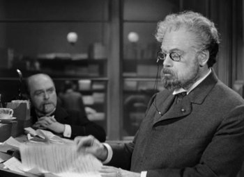 Movie still from “The Life of Emile Zola” (1937), directed by William Dieterle – An older man with a beard is reading a paper; Medium shot, Over the shoulder angle