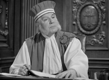 Movie still from “The Life of Emile Zola” (1937), directed by William Dieterle – An older man in a priest's outfit sitting at a table; Close Up shot, Low angle