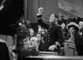 Movie still from “The Life of Emile Zola” (1937), directed by William Dieterle – An old photo of a man in a military uniform raising his arm in the air in front of an audience; Medium shot, Low angle