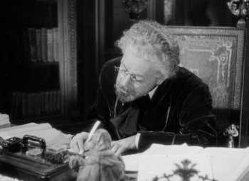 Movie still from “The Life of Emile Zola” (1937), directed by William Dieterle – An older man sitting at a desk writing on a piece of paper; Close Up shot, High angle