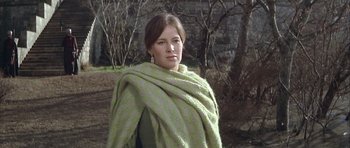 Movie still from “The Lion in Winter” (1968), directed by Anthony Harvey – A young woman wearing a green blanket standing in a wooded area; Medium shot, Low angle