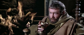 Movie still from “The Lion in Winter” (1968), directed by Anthony Harvey – A bearded man holding a metal cup in front of a fireplace; Close Up shot, High angle