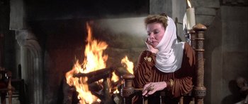 Movie still from “The Lion in Winter” (1968), directed by Anthony Harvey – A woman wearing a head scarf sitting in front of a fire; Medium shot, Over the shoulder angle