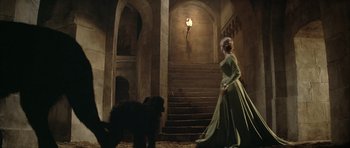Movie still from “The Lion in Winter” (1968), directed by Anthony Harvey – A woman in a green dress walking down a set of stairs with a black dog; Wide shot, Low angle