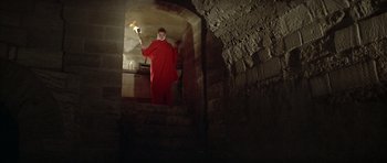 Movie still from “The Lion in Winter” (1968), directed by Anthony Harvey – A man in a red robe holding a torch in a dark room; Wide shot, High angle