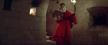 Movie still from “The Lion in Winter” (1968), directed by Anthony Harvey – A woman in a red robe holding a box and a torch; Wide shot, High angle