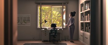 A woman standing in front of a desk looking out a window