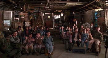 Movie still from “The Little Rascals” (1994), directed by Penelope Spheeris – A group of children sitting in a room with their hands raised; Wide shot, High angle