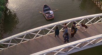 Movie still from “The Little Rascals” (1994), directed by Penelope Spheeris – A group of people walking across a bridge to a small boat; Extreme Wide shot, High angle