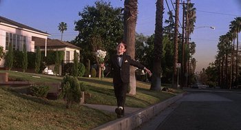 Movie still from “The Little Rascals” (1994), directed by Penelope Spheeris – A man walking down a sidewalk holding a bouquet of flowers; Wide shot, Low angle