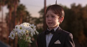 Movie still from “The Little Rascals” (1994), directed by Penelope Spheeris – A young boy in a suit and tie holding a bouquet of flowers; Close Up shot, Over the shoulder angle
