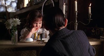 Movie still from “The Little Rascals” (1994), directed by Penelope Spheeris – A little girl sitting at a table with a glass of wine; Medium shot, Over the shoulder angle