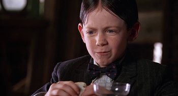 Movie still from “The Little Rascals” (1994), directed by Penelope Spheeris – A boy in a suit and bow tie eating a piece of bread; Close Up shot, Low angle