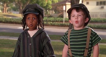 Movie still from “The Little Rascals” (1994), directed by Penelope Spheeris – Two children wearing hats standing next to each other on the grass; Medium shot, Low angle