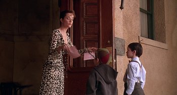 Movie still from “The Little Rascals” (1994), directed by Penelope Spheeris – A woman in a leopard print dress is handing a book to a boy; Medium shot, Over the shoulder angle