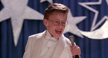 Movie still from “The Little Rascals” (1994), directed by Penelope Spheeris – A young boy wearing a white suit and holding a microphone; Close Up shot, High angle