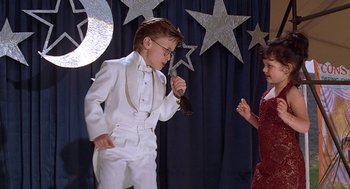 Movie still from “The Little Rascals” (1994), directed by Penelope Spheeris – A boy and a girl are dressed up and singing together; Medium shot, Low angle