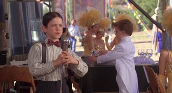 Movie still from “The Little Rascals” (1994), directed by Penelope Spheeris – A young boy holding a microphone in front of a crowd; Medium shot, Over the shoulder angle