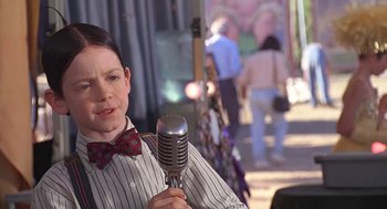 Movie still from “The Little Rascals” (1994), directed by Penelope Spheeris – A young boy holding a microphone in his hand; Close Up shot, Over the shoulder angle