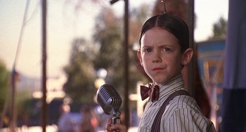 Movie still from “The Little Rascals” (1994), directed by Penelope Spheeris – A young boy holding an old fashioned microphone in his hand; Close Up shot, Over the shoulder angle