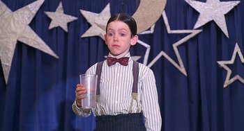 Movie still from “The Little Rascals” (1994), directed by Penelope Spheeris – A boy in a striped shirt and bow tie holding a cup; Medium shot, Low angle