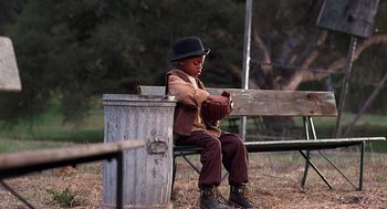 Movie still from “The Little Rascals” (1994), directed by Penelope Spheeris – A boy sitting on top of a wooden bench; Wide shot, Low angle
